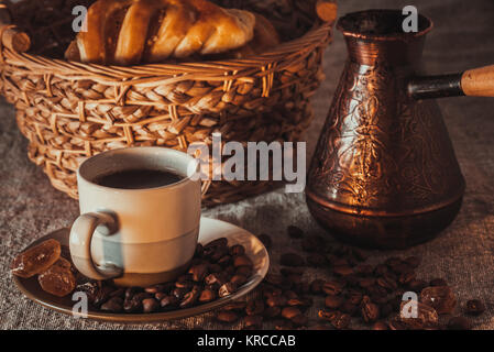 Tasse de café sur le textile avec les légumineuses, le sucre candi, pots, panier et gâteau Banque D'Images