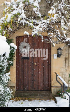 Couronne de Noël sur une maison en pierre de Cotswold porte avant en bois en décembre tandis que sa neige. Chipping Campden, Cotswolds, Gloucestershire, Angleterre Banque D'Images