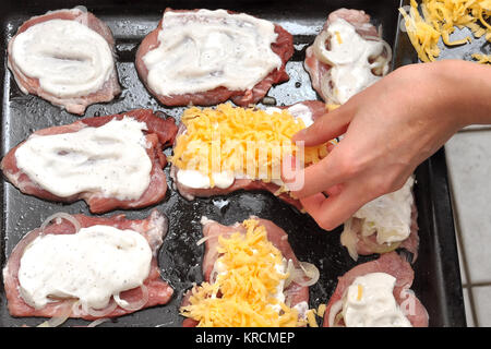 Main femme saupoudre de fromage râpé les côtelettes de porc crus portant sur une plaque de cuisson pour la cuisson des processus étape par étape. Haut de la vue, télévision lay. Banque D'Images