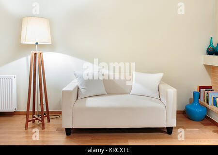 Un petit canapé deux places avec deux petits oreillers et un socle en bois lampe sur un plancher en chêne. Banque D'Images