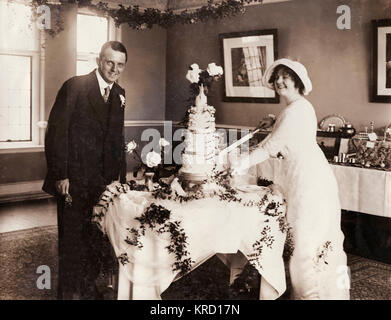 Scène à la réception de mariage de Dan et Everard Dollis Brook, artistes interprètes ou exécutants dans l'Pelissier Follies. Le mariage a lieu à l'église paroissiale de Finchley, au nord de Londres. Ici l'épouse, c'est couper le premier morceau d'un gâteau à trois niveaux. Date : vers 1909 Banque D'Images