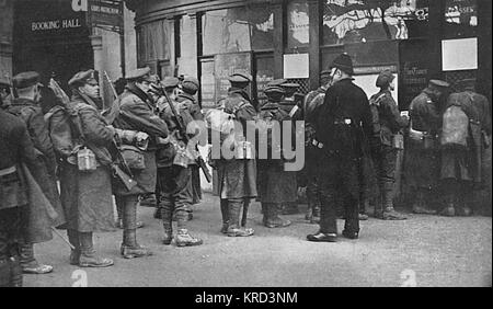 Hommes tout juste d'arriver à la gare de Waterloo à partir de l'achat des tranchées des billets à la centrale de réservation pour les voyages à leurs maisons de banlieue. Une scène typique dans les gares de Londres pendant la Première Guerre mondiale. Date : 1914 Banque D'Images