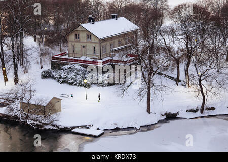 Un homme reprend sa course à travers un paysage couvert de neige, passé Cafe Kajak, Rålambshovspark Kungsholmen. Au premier plan est la Riddarfjärden congelé Banque D'Images