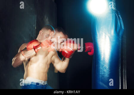 Male boxer boxing sac de frappe dans l'éclairage dramatique avec edgy dans un studio sombre Banque D'Images