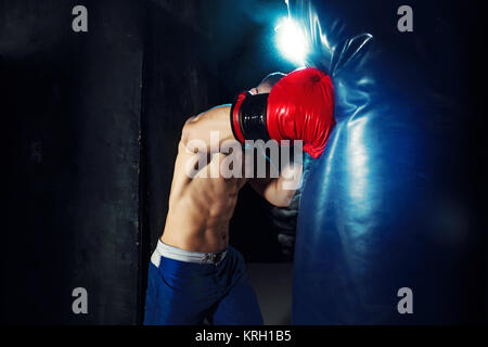 Male boxer boxing sac de frappe dans l'éclairage dramatique avec edgy dans un studio sombre Banque D'Images