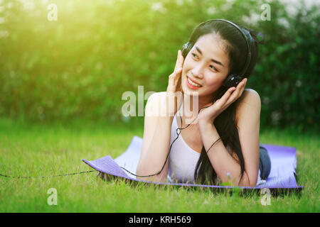 Jeune femme à l'écoute de la musique avec des écouteurs et portant sur un champ d'herbe Banque D'Images