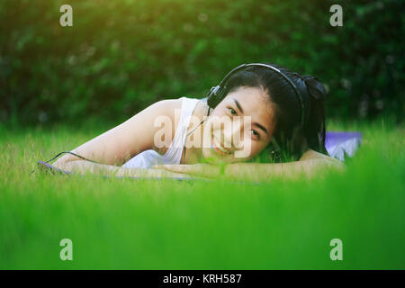 Jeune femme à l'écoute de la musique avec des écouteurs et portant sur un champ d'herbe Banque D'Images