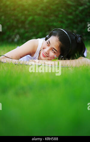 Jeune femme à l'écoute de la musique avec des écouteurs et portant sur un champ d'herbe Banque D'Images