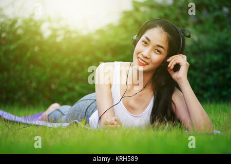 Jeune femme à l'écoute de la musique avec des écouteurs et portant sur un champ d'herbe Banque D'Images