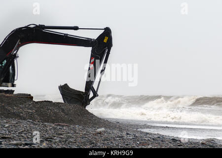 L'excavatrice fonctionne avec un seau rempli de pierres sur le bord de la mer dans une tempête. Banque D'Images