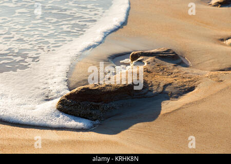 Vue rapprochée d'une vague de toucher un grand rocher calcaire incorporée dans le sable d'une plage. Banque D'Images