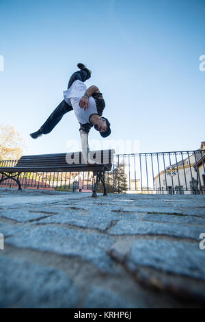 Young man doing handstand sur un banc dans la rue tout en faisant parkour. Banque D'Images