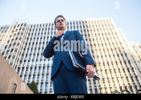 Jeune homme en costume élégant posant avec l'ordinateur portable dans sa main à la voiture. Banque D'Images