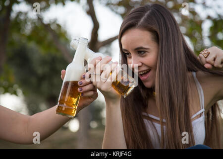 Deux jeunes femmes rire posant sur pelouse au parc et le grillage avec les bouteilles de bière s'amusant. Banque D'Images