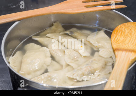 Non-authentique traditionnelle polonaise organisée la veille de Noël dans l'induction de métal moderne pierogies pot rempli d'eau, pendant la préparation- prêt à bouillir. Banque D'Images