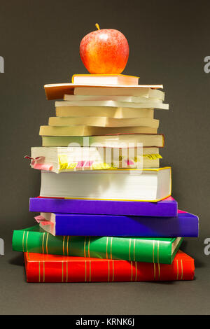 Concept de l'éducation. Pile de livres scolaires avec une pomme rouge en haut en face de fond gris foncé Banque D'Images