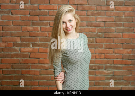 Portrait d'une blonde dans un pull léger. L'article contre le mur de brique rouge, souriant et posant pour l'appareil photo. ses longs cheveux est mis dans une direction Banque D'Images