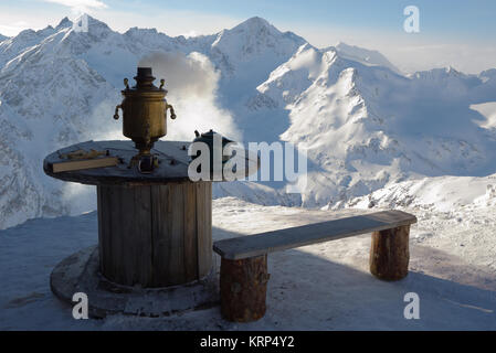 Un banc en bois à côté d'une table en bois sur laquelle se trouve le sex samovar, théière, tasse de thé. Contre la montagne enneigée des pics. Banque D'Images