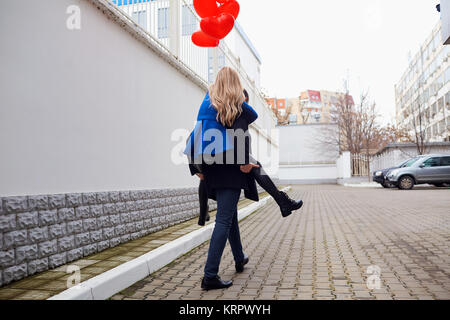 Fille sur le dos de gars avec des ballons coeur rouge dans la rue. Banque D'Images