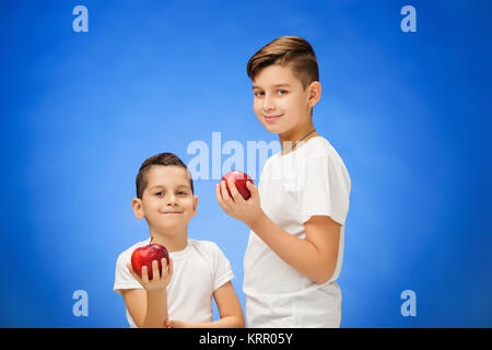 Beaux petits garçons avec deux pommes rouges. Studio portrait sur fond bleu Banque D'Images