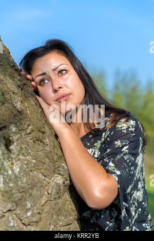 Portrait young woman leaning against tree trunk Banque D'Images