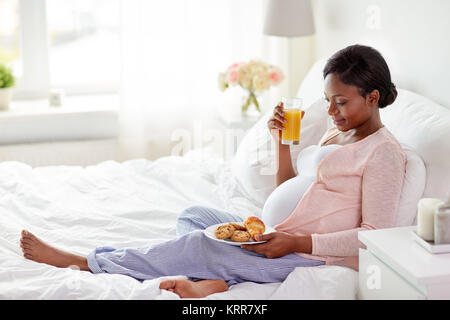 Femme enceinte avec du jus d'orange et pâtisseries au lit Banque D'Images