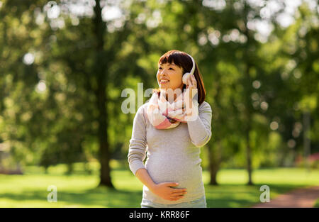 Happy pregnant asian woman in headphones at park Banque D'Images