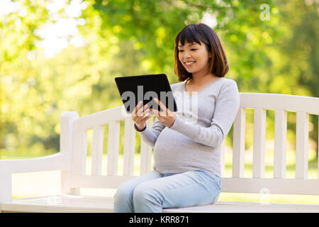 Happy pregnant asian woman with tablet pc at park Banque D'Images