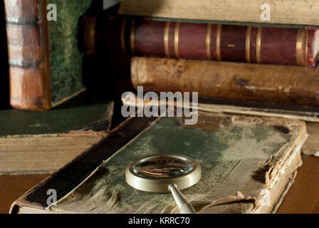 Un vieux livre dans une couverture en lambeaux et une loupe sur une table libre sur un arrière-plan flou d'autres vieux livres Banque D'Images