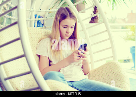 Fille blonde avec phone sitting in chair Banque D'Images