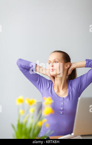 Travailler trop dur - jeune femme travaillant sur un ordinateur dans un bureau, avoir mal au dos, d'être débordé de travail, assis trop, mettre trop l'accent sur ses yeux,.. Banque D'Images