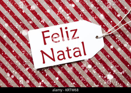 Une étiquette sur un carton rouge à rayures marron et papier d'emballage. Background avec des flocons de neige. Tag avec ruban. Texte portugais Feliz Natal signifie Joyeux Noël Banque D'Images