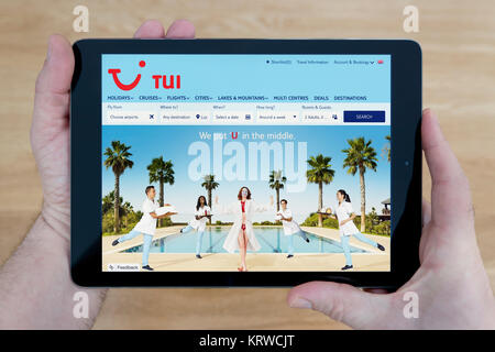 Un homme regarde la TUI site sur son iPad tablet device, tourné contre une table en bois page contexte (usage éditorial uniquement) Banque D'Images