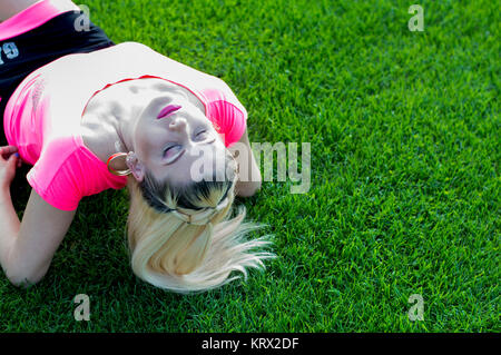 La blonde qui a rejeté en arrière la tête couchée sur le terrain de football Banque D'Images