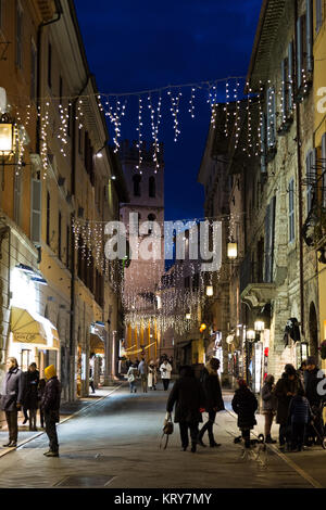 Vue de la rue principale à Assise (Ombrie) pendant la période de Noël, avec les gens à faire leurs achats, décorations de lumière et le clocher de la Piazza del Comune Banque D'Images