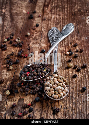 Poivre épices secs pois noir et blanc parfumé, parfumé, sec pour la cuisson versé dans deux cuillères se trouve sur un fond de bois Banque D'Images