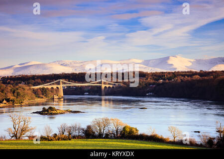 Vue panoramique sur le détroit de Menai avec Thomas Telford, pont suspendu de Menai et neige de l'hiver sur les montagnes de Snowdonia. Menai Bridge Anglesey au nord du Pays de Galles UK Banque D'Images