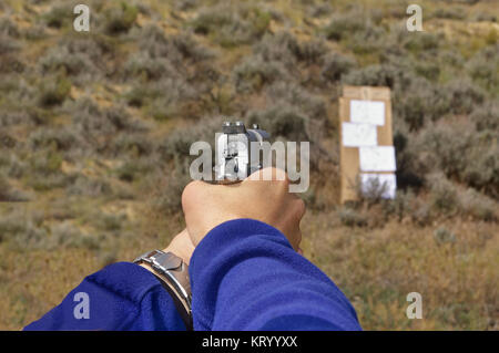 1911-type pistolet semi-automatique dans une main courante visant à un carton/papier cible sur une plage en plein air Banque D'Images