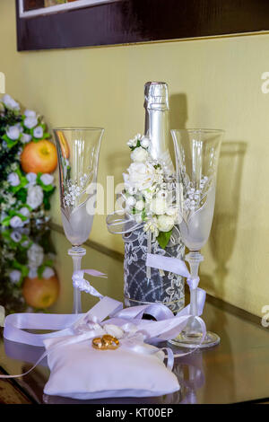 Les anneaux de mariage sur de beaux coussins dans le contexte de fêtes de verres à vin et champagne. Symboles de mariage, attributs. Banque D'Images