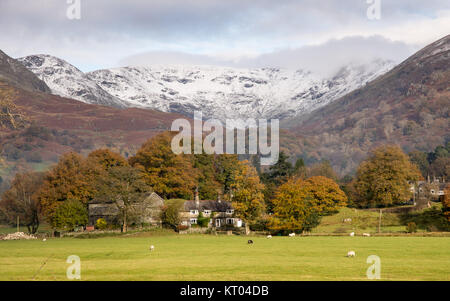 C'est de la neige sur les sommets des montagnes Hart Crag et Fairfield, au-dessus de la vallée de la rivière Rathay, où les moutons paissent à côté d'une ferme et d'arbres di Banque D'Images