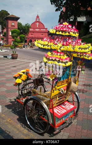 Melaka, Malaisie - 25 novembre, 2004 : Trishaw colorées décorées de fleurs peintes en rouge et l'Église du Christ dans l'arrière-plan Banque D'Images