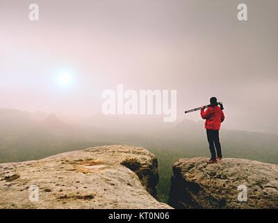 Photographe pensez à photo sur le pic de production dans les montagnes brumeuses. Photographie à l'aube, la vallée ci-dessus cachés dans le brouillard lourd. Vue d'un paysage brumeux Banque D'Images