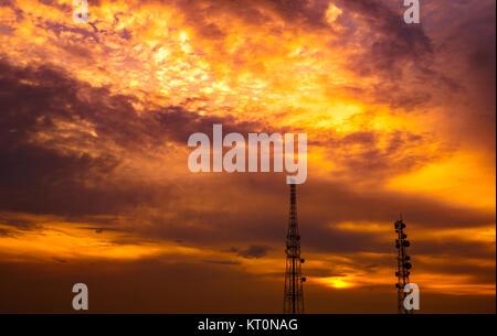 Deux tours de télécommunication sur sombre dramatique-orange Ciel et nuages background Banque D'Images