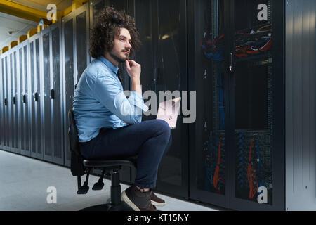 Jeune technicien travaillant sur un ordinateur portable à côté de racks de serveur noir Banque D'Images