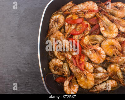 Crevettes fraîches cuites avec oignons et tomates crevettes fraîches cuites / avec de la tomate et les oignons servis dans une assiette sur un sol en bois () Contexte En céramique noire Banque D'Images