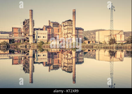 Ancienne usine. Usine de fabrication de produits chimiques. Cheminées,Tuyaux,réservoir de stockage et le pylône électrique. Reflète dans la rivière.Photo en style vintage Banque D'Images