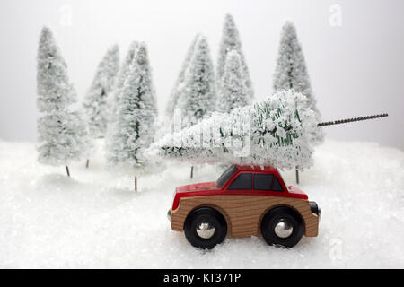 Voiture rouge portant un arbre de Noël dans une forêt miniature couvert de neige Banque D'Images