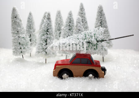 Voiture rouge portant un arbre de Noël dans une forêt miniature couvert de neige Banque D'Images