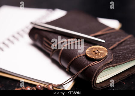 Couvert de cuir vintage ntoebook sur un journal ouvert sur une planche en bois foncé Banque D'Images