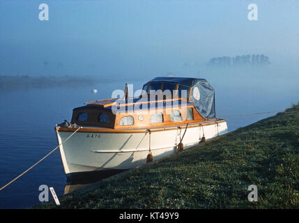 Petit motor cruiser amarré sur la banque du fleuve Bure, Norfolk, avec brouillard tôt le matin Banque D'Images